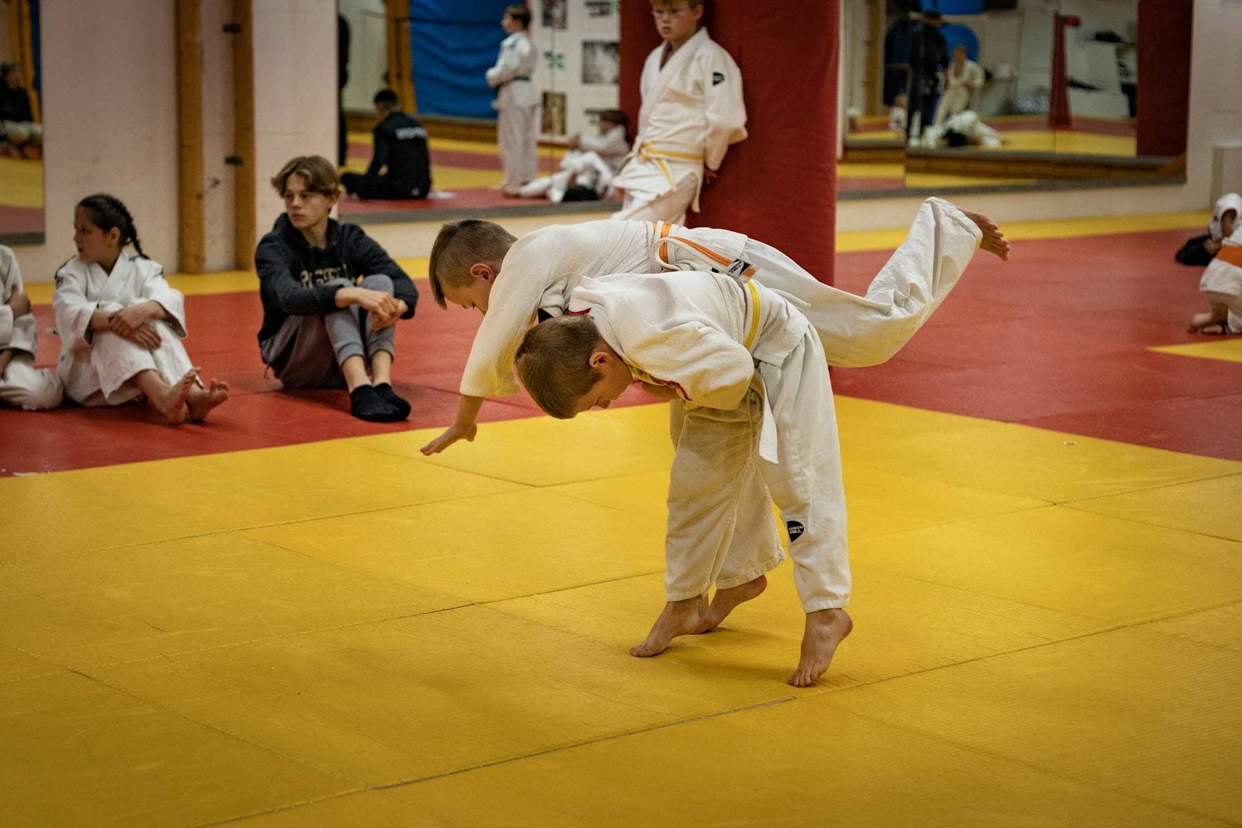 Kinder im Judoanzug: ein Junge wirft seinen Partner, die anderen schauen vom Mattenrand zu