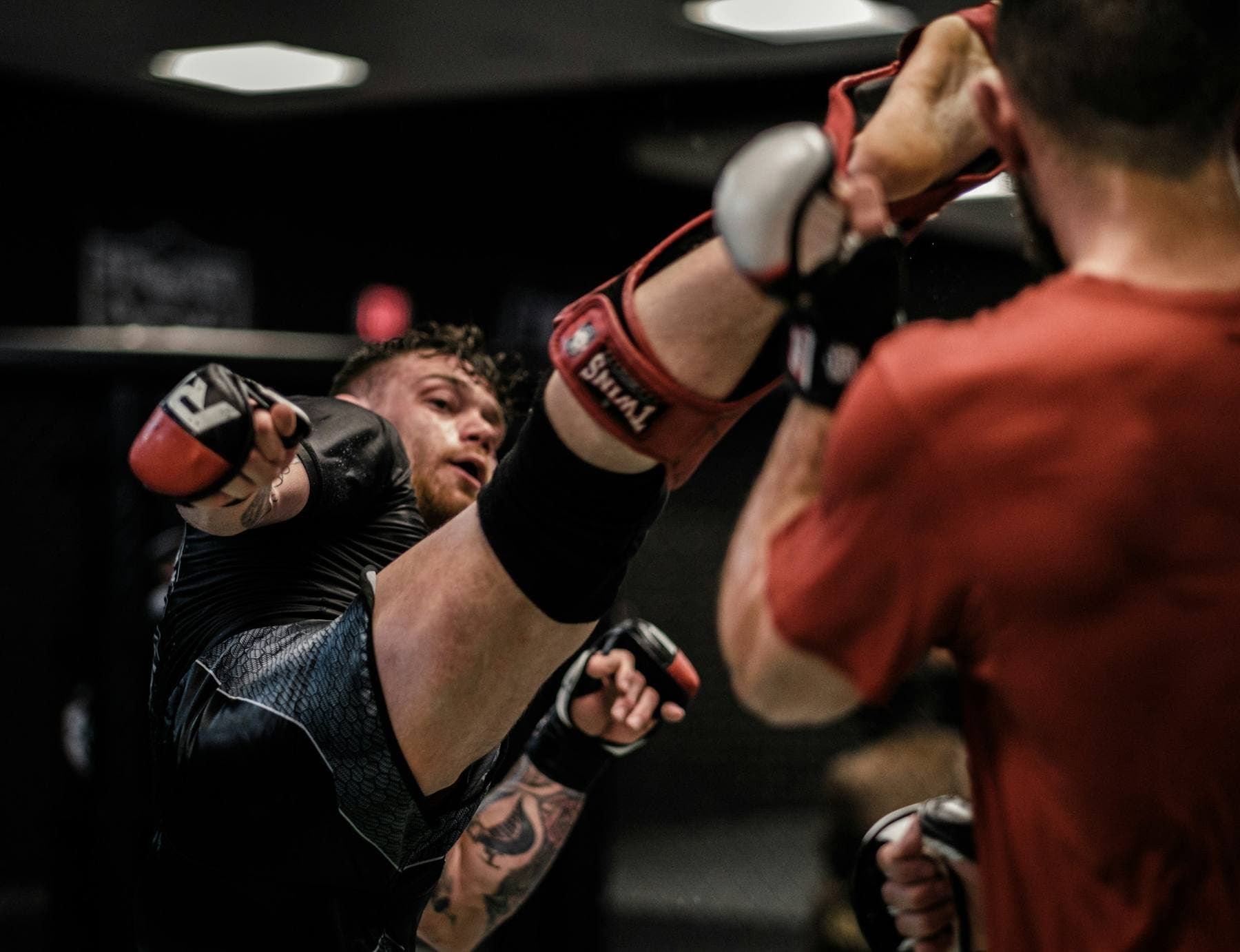 Hoher Tritt beim Sparring in MMA-Handschuhen in einer dunklen Trainingshalle
