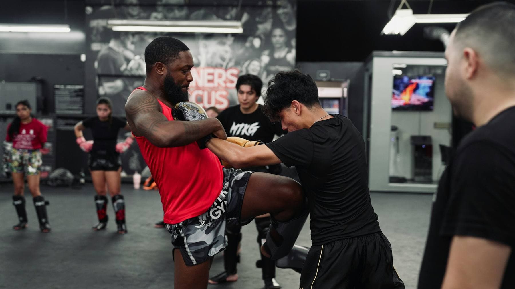 Clinch im Muay-Thai-Training: ein Kämpfer in Thaiboxhose setzt das Knie gegen die Pratze seines Partners